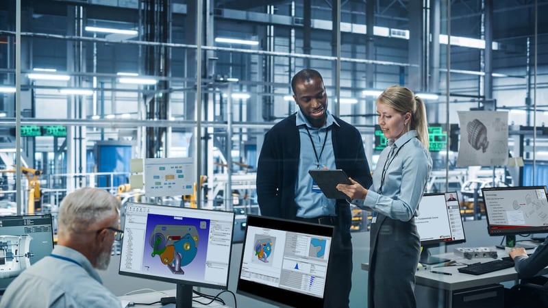 Group of engineers looking at tablet in the background with older male in the foreground looking at a desktop computer with Sigmetrix CETOL on screen