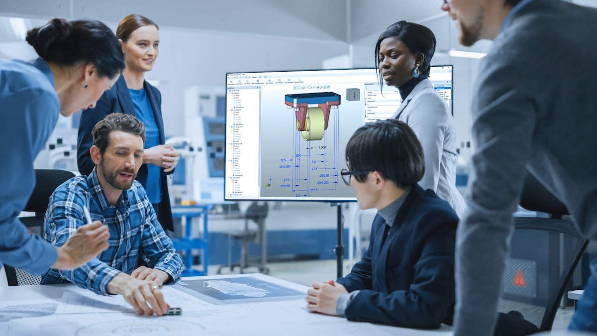 Professional team sitting at table looking at blueprints with computer screen in background