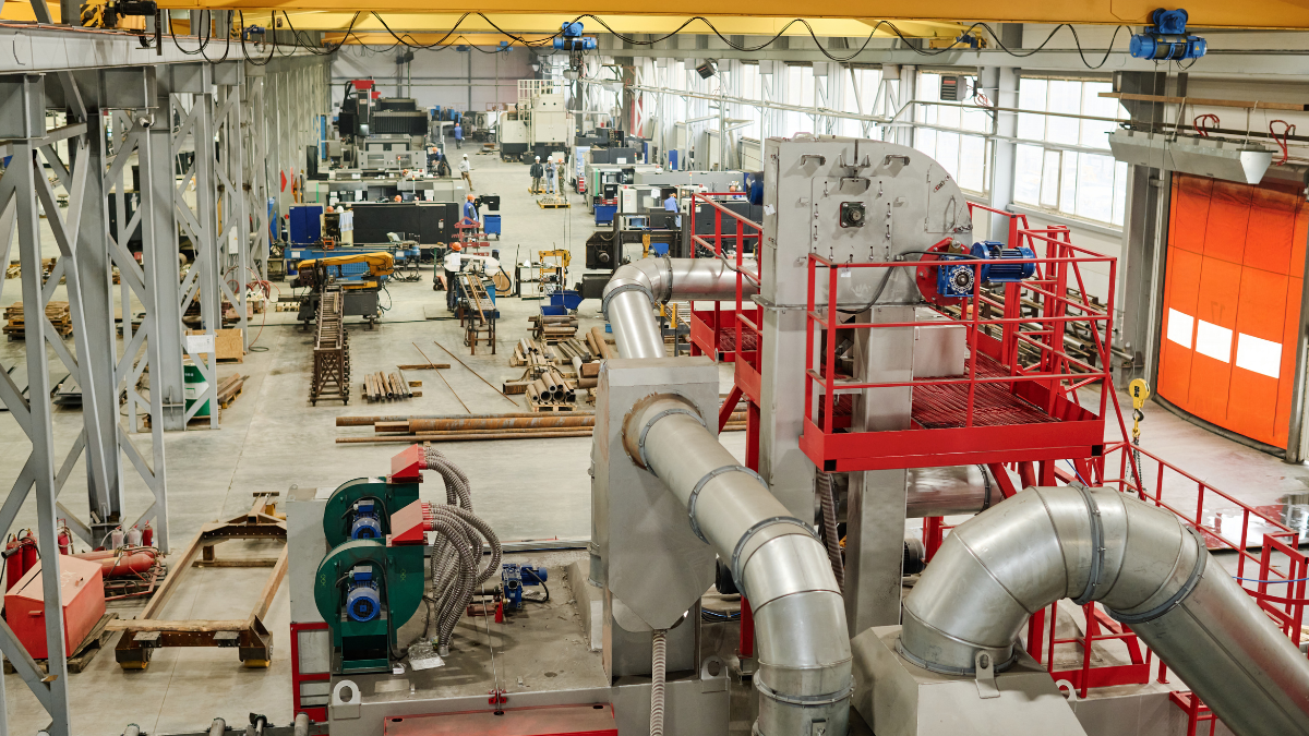 Model based definition in action on a modern manufacturing shop floor, with industrial machinery, large ducting/piping, and production equipment in a factory facility.